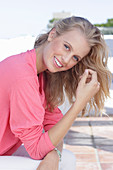 A young blonde woman wearing a pink blouse with gigot sleeves and white trousers