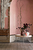 Kannen und Blumenstrauß auf rundem Tisch vor verfallener Wand