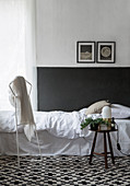 Bett vor weißer Wand mit schwarzem Sockel auf grafischem Teppich