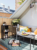 Sunny seating area on inverted dormer roof terrace with honeycomb tiles, bench and table