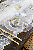 Gedeckter Tisch mit Glastellern, goldenem Besteck und Spitze