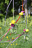 Flowers in screw top jars suspended from ribbons