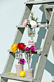 Blumen in Vasen aus Trinkgläsern mit Betonsockel auf einer Leiter