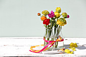 Vier Glasflaschen mit Geschenkband und bunten Frühlingsblumen
