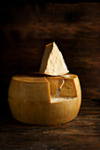 A wheel of Parmesan cheese with a slice cut out
