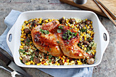 Half roast chicken in a dish with rice, corn and mushrooms