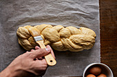 A braided loaf being spread with egg yolk