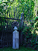Urn on top of granite pillar in front of rustic fence made from branches
