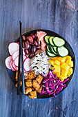 Buddha bowl with basmati rice, mango, fried tofu, purple cabbage, radishes, olives, pickled ginger and seaweed