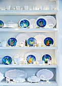 White china and blue decorative plates with winter motifs on shelves decorated with fairy lights