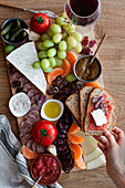 Persons eating snacks, sliced of meat, vegetables, fruits and glass of red wine