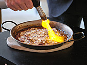Chef using gas burner while cooking rice with octopus carpaccio and pepper aioli in metal pan