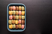 Colorful macaroons displayed inside blue container on black background