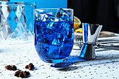 Blue cocktail with ice cubes and barmen tools on table