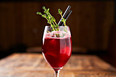 Red berry cocktail decorated with green rosemary in modern glass with tubes on wooden table in bar