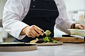 Chef preparing meat steak with green powder and herbs served on ceramic plate