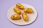 Eclairs with golden icing placed on plate on lilac background