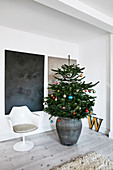 Decorated Christmas tree and Tulip chair in front of abstract paintings on wall