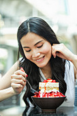 Junge Asiatin isst Tiramisu-Erdbeer-Eisbecher in Straßencafe in Bangkok