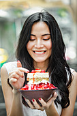 Young Asian woman eats a tiramisu strawberry ice cream sundae in a street cafe in Bangkok