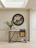 Round, abstract painting on wall above console table in interior with skylights