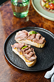 Tasty ham in row on crispy toasts on black plate on wooden table