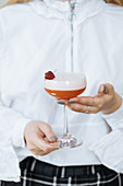 Waiter holding delicious red cocktail in stylish glass decorated with fresh raspberry