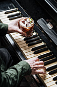 Man playing piano with one hand and holding glass with cocktail in other hand