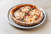 Baked pizza served with cheese and herbs on table