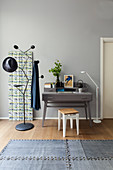 Grey writing desk next to decorative wall panel and designer coat stand