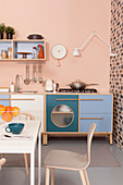 Kitchen counter with blue, white and turquoise cabinets against pastel-pink wall