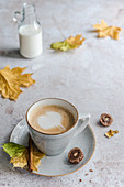 Cappuccino with a milk foam heart surrounded by autumn leaves