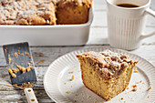 A piece of crumb cake served on a white plate with a white coffee mug filled with coffee