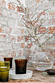 Branch in clear spherical vase and coloured glass vases in front of brick wall