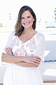 A long-haired woman wearing a white summer dress with colourful embroidery detail