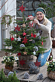 Frau schmückt Nordmanntanne mit roten Holzsternen und Zapfen als Weihnachtsbaum
