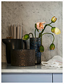 Poppy buds coming into flower in rustic vase next to candles in jug