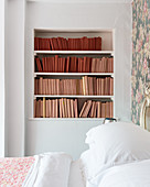 Books with covers in shades of red and pink on shelves in bedroom