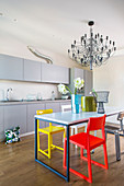 Schlichte graue Küchenzeile davor Esstisch mit verschiedenfarbigen Designerstühlen
