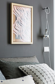 Abstraktes Wandbild und Glühbirne am Kabel als Nachttischleuchte über Bett