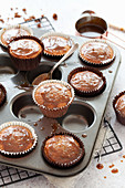 Sticky toffee cupcakes in a baking tin with sticky toffee sauce