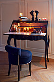 Lit tealights on Rococo-style bureau and chair with blue upholstery