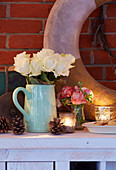 Zapfen, Teelichtgläser und weißer Rosenstrauß als Deko auf Sideboard