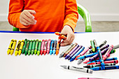 Child arranging coloured wax crayons on canvas
