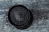 Poppyseeds in a black bowl against a black background