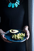 Frau hält Teller mit Avocado-Brot in den Händen