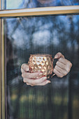 Hands behind a window holding a copper mug