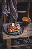 Almond croissant and cup of coffee served on an old rustic wooden chair
