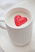 A cup of white hot chocolate with whipped cream and two pink heart marshmallows