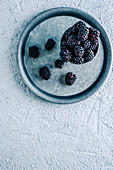 Cup with ripe blackberries placed on metal tray on plaster surface